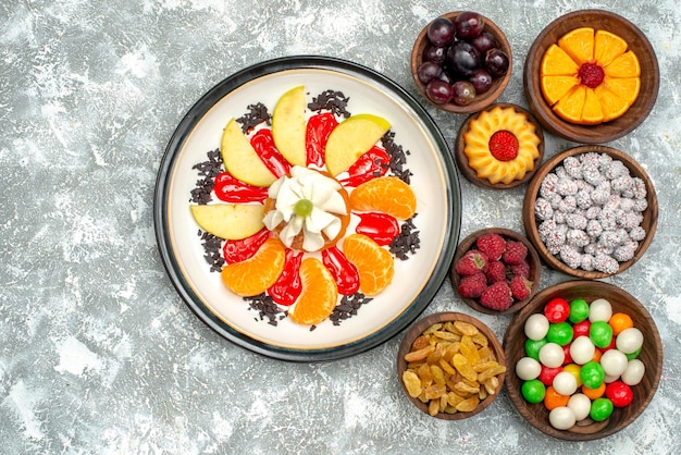 Vista superior pequeño pastel cremoso con frutas en rodajas, caramelos y pasas en superficie blanca pastel dulce de frutas pastel galleta de azúcar