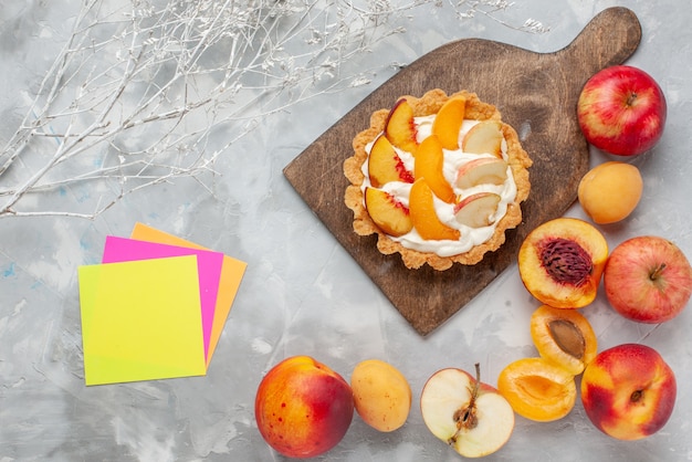 Vista superior pequeño pastel cremoso con frutas en rodajas y crema blanca junto con frutas frescas en el escritorio blanco claro pastel de frutas galleta crema dulce hornear