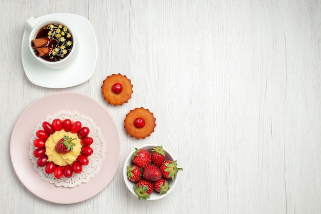 Foto gratuita vista superior pequeño pastel cremoso con frutas y taza de té en el escritorio blanco