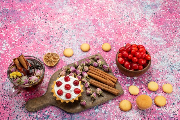 Vista superior pequeño pastel cremoso con té de galletas de canela y frutos rojos en el escritorio púrpura fruta dulce