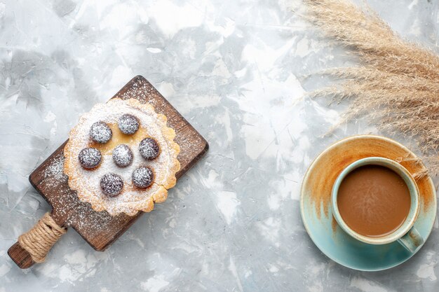 Vista superior pequeño pastel delicioso con azúcar de frutas en polvo con café con leche en la mesa de luz pastel pastel de galletas azúcar dulce