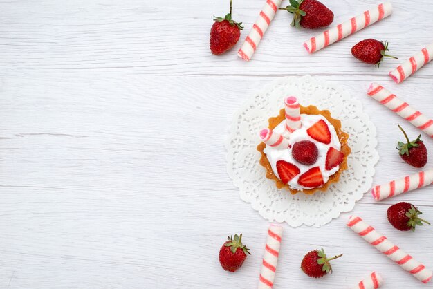 Vista superior pequeño pastel delicioso con crema y fresas en rodajas palo dulces sobre fondo blanco pastel baya dulce azúcar hornear