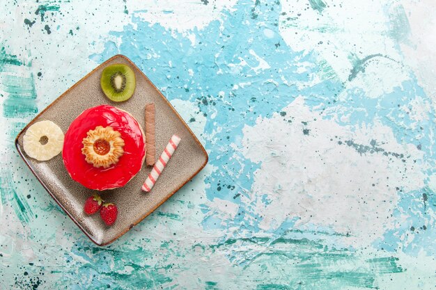 Vista superior pequeño pastel delicioso con crema roja sobre fondo azul claro pastel galleta dulce azúcar pastel té galleta