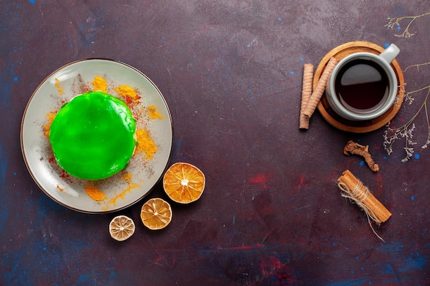 Vista superior del pequeño pastel delicioso con crema verde y una taza de té en la superficie oscura