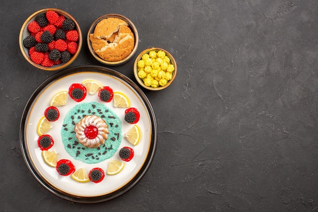 Vista superior pequeño pastel delicioso con rodajas de limón y caramelos en el fondo oscuro pastel de galletas fruta cítrica galleta dulce