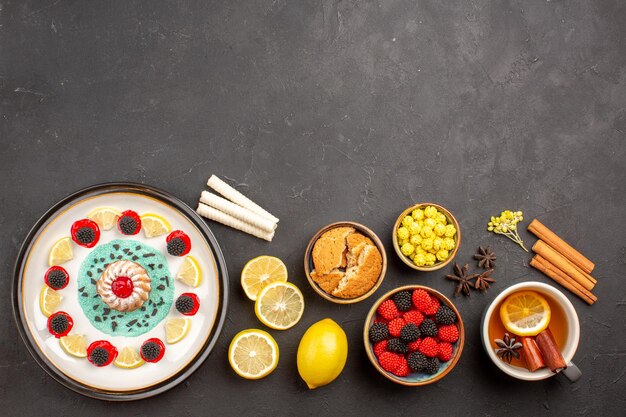 Vista superior pequeño pastel delicioso con rodajas de limón y una taza de té en el fondo oscuro galleta de fruta cítrica galleta dulce pastel