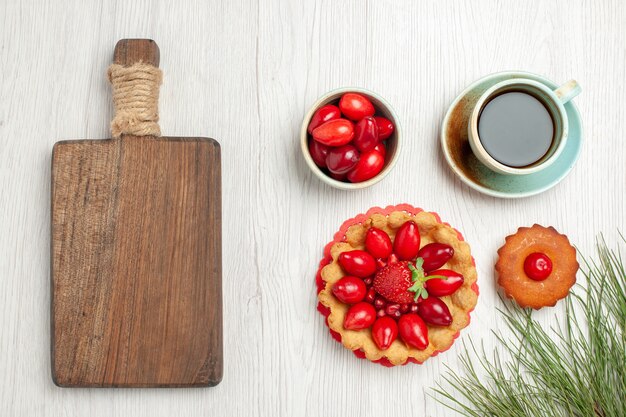 Vista superior del pequeño pastel con frutas y una taza de té en el escritorio blanco