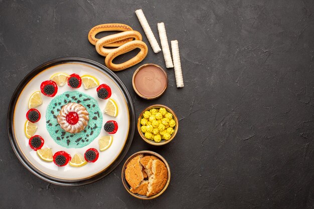 Vista superior pequeño pastel de galletas con rodajas de limón y caramelos en el fondo oscuro pastel galleta dulce fruta cítrica galleta