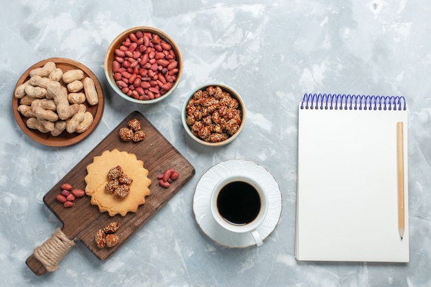 Vista superior del pequeño pastel con pistachos, taza de té y nueces sobre superficie blanca clara