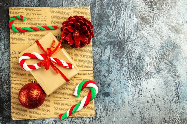 Vista superior pequeño regalo atado con caramelos de Navidad de cinta roja en periódico sobre superficie gris