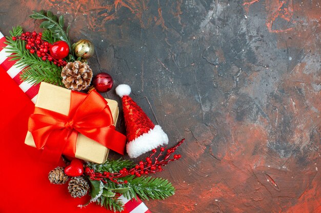 Vista superior pequeño regalo atado con cinta roja mini sombrero de santa rama de árbol de navidad en el espacio de copia de mesa rojo oscuro