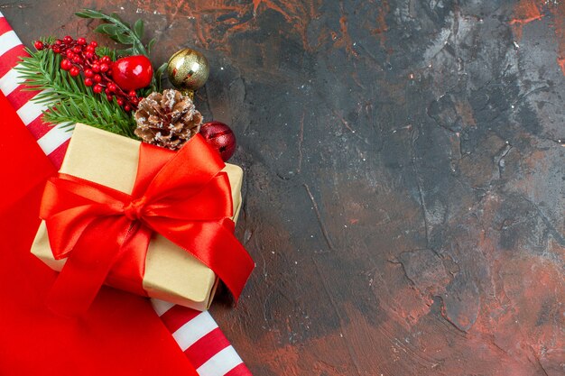 Vista superior pequeño regalo atado con cinta roja rama de árbol de Navidad en mesa de color rojo oscuro con lugar de copia