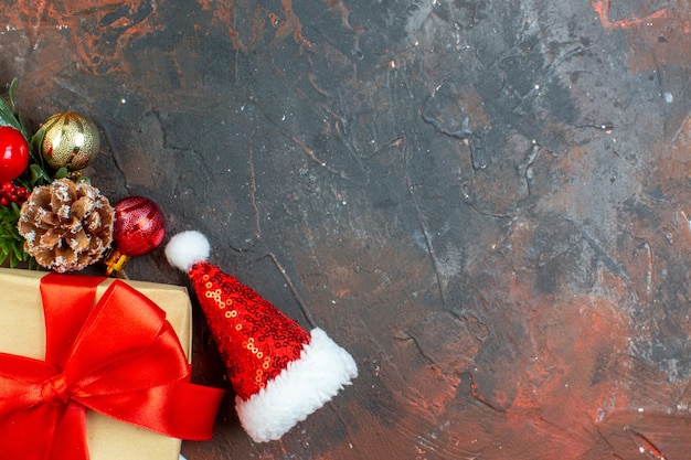 Vista superior pequeño regalo atado con cinta roja rama de árbol de Navidad mini gorro de Papá Noel en el lugar de copia de mesa rojo oscuro