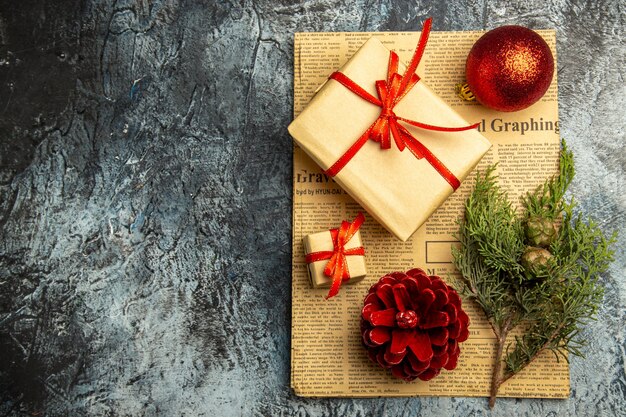Vista superior pequeño regalo atado con cinta roja rama de pino de bola de Navidad roja en periódico sobre superficie oscura