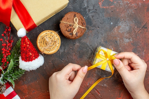 Foto gratuita vista superior pequeño regalo en mano femenina galletas de sombrero de santa en mesa rojo oscuro