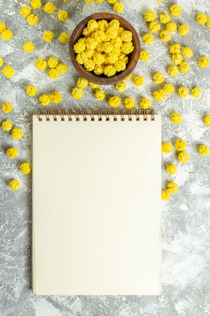 Vista superior de pequeños caramelos amarillos con bloc de notas en té de caramelo dulce de color de superficie blanca