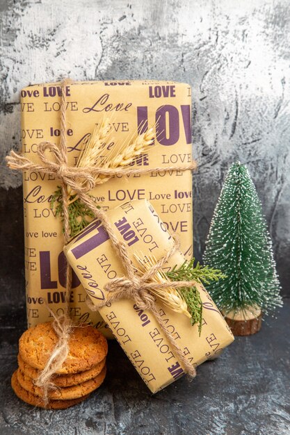 Vista superior de pequeños y grandes regalos llenos de pie en la pared y árbol de Navidad de galletas sobre fondo oscuro