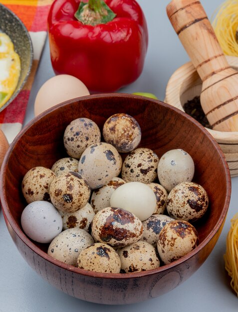 Vista superior de pequeños huevos de codorniz en un tazón de madera con pimiento rojo sobre fondo blanco.