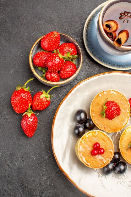 Vista superior pequeños panqueques deliciosos con frutas y una taza de té en el escritorio gris pastel pastel de frutas