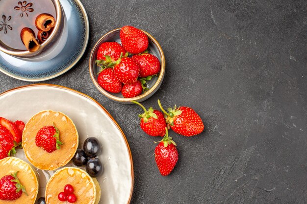 Vista superior pequeños panqueques deliciosos con frutas y una taza de té en la superficie gris pastel pastel de frutas