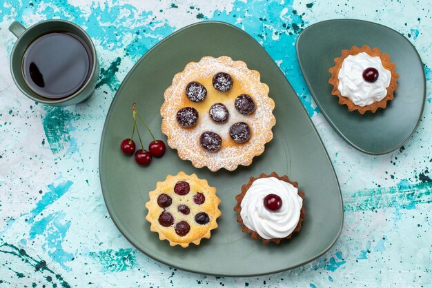 Vista superior de pequeños pasteles con crema de frutas de azúcar en polvo en té dulce de frutas de pastel de mesa azul claro