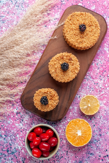 Foto gratuita vista superior de pequeños pasteles deliciosos con cornejos sobre superficie rosa claro