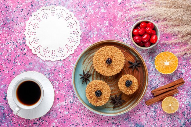 Vista superior de pequeños pasteles deliciosos con cornejos y té en la superficie de color rosa claro