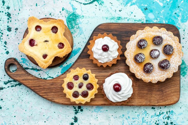 Vista superior de pequeños pasteles deliciosos con crema y frutas en la mesa de luz pastel galleta crema de té dulce