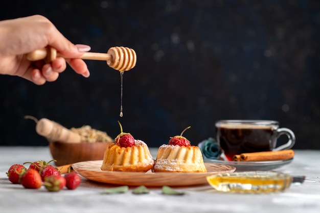 Una vista superior de pequeños pasteles deliciosos obteniendo un poco de miel con fresas rojas, canela y galleta de pastel de té