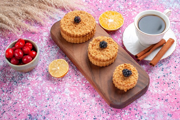 Vista superior de pequeños pasteles deliciosos redondos formados con canela y té sobre una superficie rosa claro