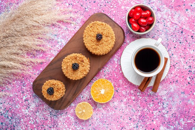 Vista superior de pequeños pasteles deliciosos redondos formados con canela y té en la superficie de color rosa claro