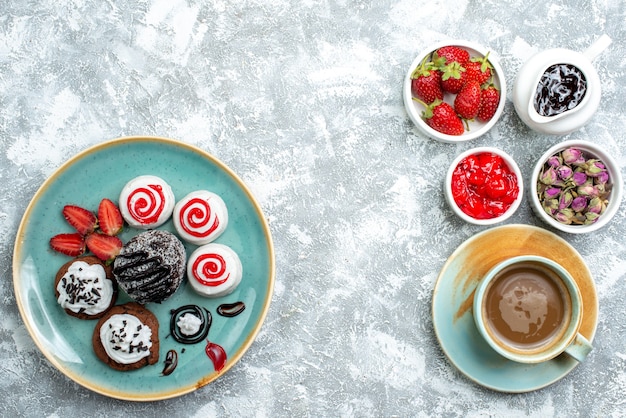 Vista superior de pequeños pasteles dulces con frutas y una taza de café sobre un fondo blanco pastel de galletas de galletas dulces pastel de azúcar