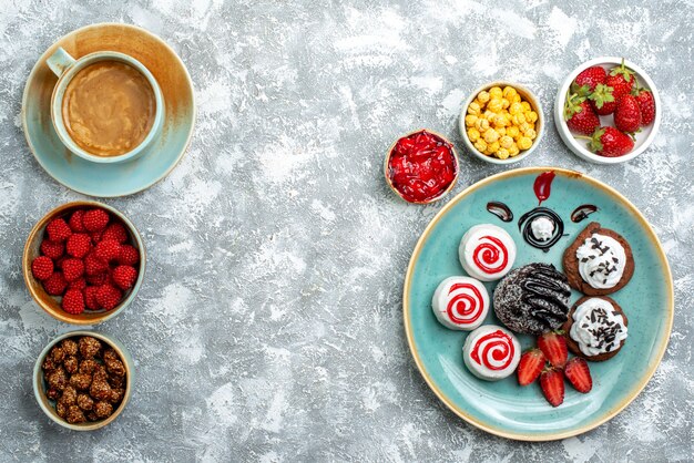 Vista superior de pequeños pasteles dulces con taza de café y caramelos sobre un fondo blanco pastel de tarta galleta dulce galleta de azúcar