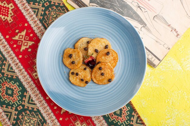 Vista superior de pequeños pasteles de galleta dentro de la placa azul en la mesa amarilla, hornear pasteles de té dulce