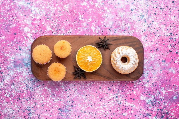 Foto gratuita vista superior de pequeños pasteles con rodaja de naranja en la superficie rosa