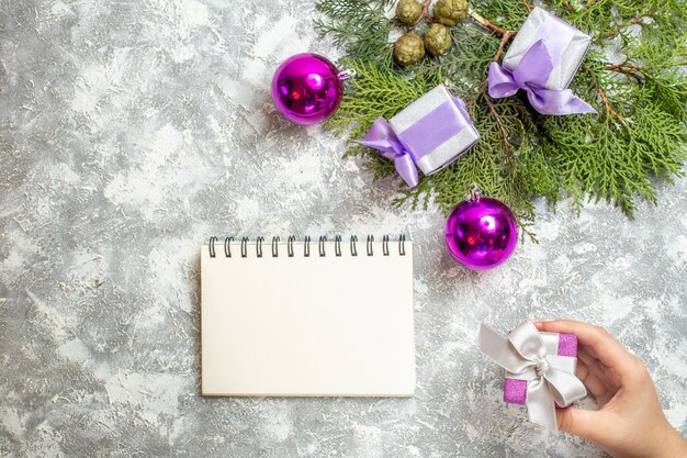 Vista superior pequeños regalos ramas de pino árbol de navidad juguetes cuaderno regalo en mano femenina sobre superficie gris