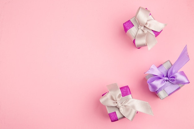 Vista superior de pequeños regalos en superficie rosa.