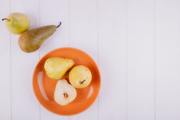 Vista superior de peras maduras frescas en un plato de cerámica naranja sobre fondo blanco con espacio de copia