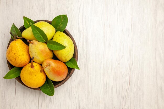 Vista superior peras melosas frescas frutas dulces dentro de la placa en el escritorio blanco frutas amarillo dulce maduro maduro