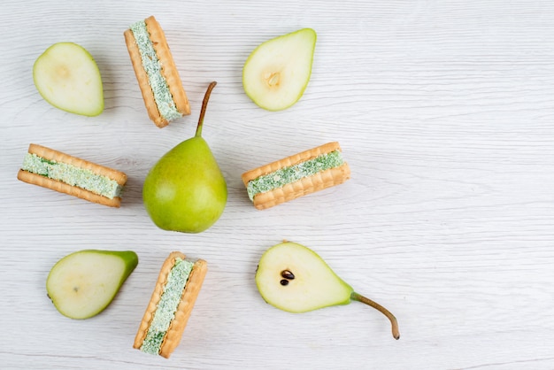 Una vista superior de peras verdes frescas en rodajas y enteras con galletas de frutas en el escritorio blanco color de fruta