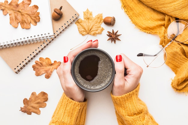 Vista superior de la persona que sostiene la taza de café con hojas de otoño