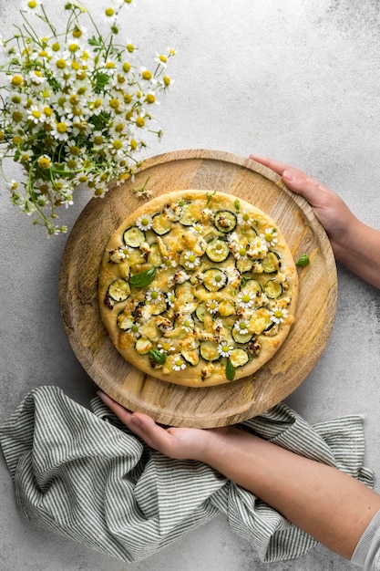 Vista superior de la persona que tiene una deliciosa pizza cocida con ramo de flores de manzanilla