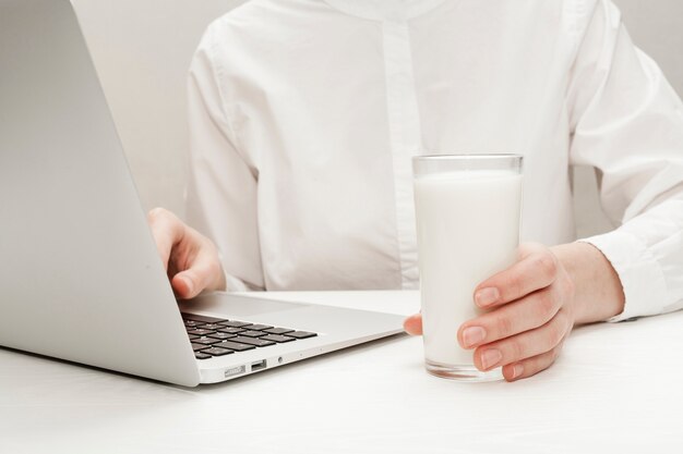 Vista superior persona que trabaja en la computadora portátil mientras sostiene un vaso de leche