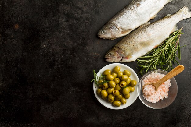 Vista superior de pescado, aceitunas y planta aromática