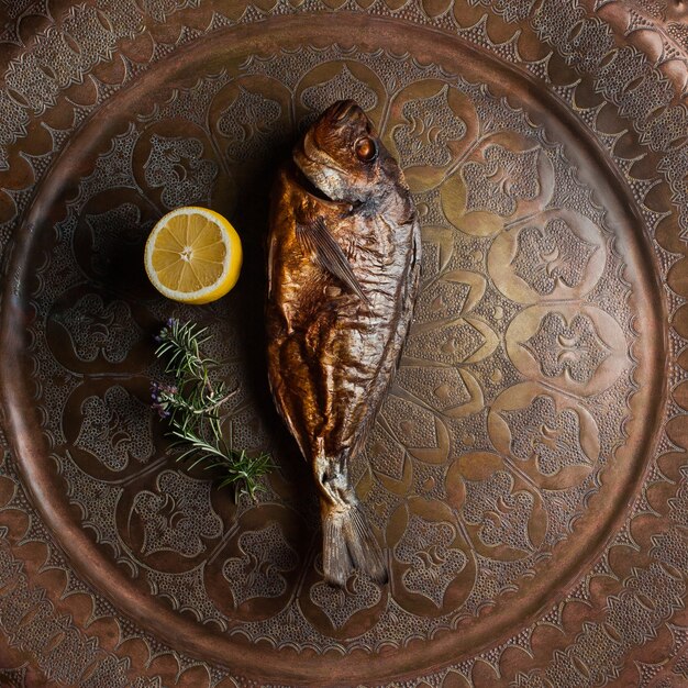 Vista superior de pescado ahumado con hojas de limón y romero en bandeja de cobre