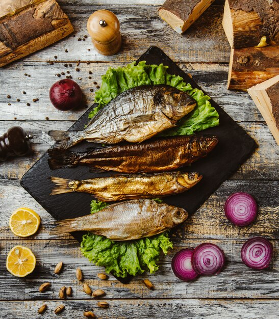 Vista superior de pescado ahumado servido con lechuga en una tabla de servir negra