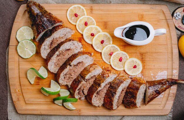 Vista superior pescado al horno relleno de lavangi y rodajas de lima y limón en un tablero