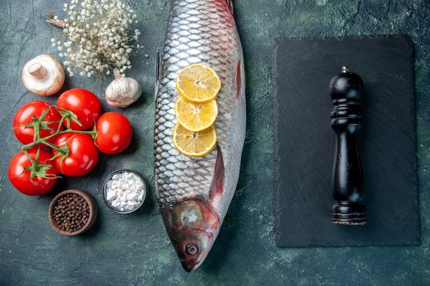 Foto gratuita vista superior de pescado crudo fresco con limón y tomates sobre fondo azul oscuro