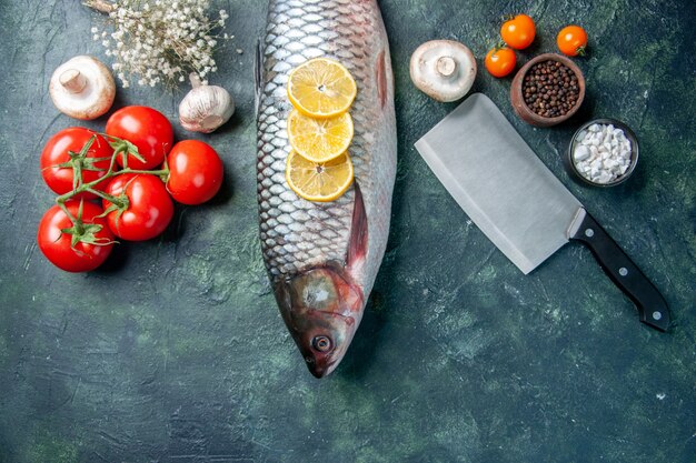 Vista superior de pescado crudo fresco con limón y tomates sobre fondo azul oscuro