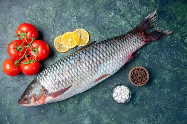 Vista superior de pescado crudo fresco con tomates y rodajas de limón sobre fondo azul oscuro